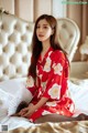 A woman in a red kimono sitting on a bed holding a fan.