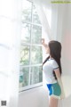 A woman standing in front of a window looking out the window.