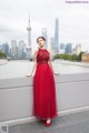 A woman in a red dress leaning against a wall.