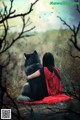 A woman in a red cloak sitting next to a black wolf.