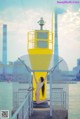 A naked woman standing on a pier next to a yellow lighthouse.