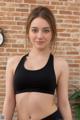 A woman in a black sports bra top posing in front of a brick wall.