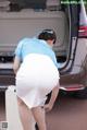 A woman in a white skirt is putting something in the trunk of a car.