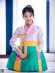 A young girl wearing a colorful hanbok sitting on a bed.