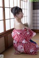 A woman in a red and white kimono sitting on the floor.