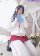 A woman in a white sweater and red skirt holding a book.