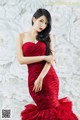 A woman in a red dress posing in front of a wall of paper flowers.