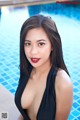 A woman in a black bathing suit posing by a swimming pool.