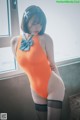 A woman in an orange bodysuit and black stockings posing by a window.