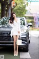 A woman in a white dress standing next to a car.