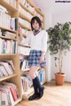 A woman in a school uniform standing in front of a bookshelf.